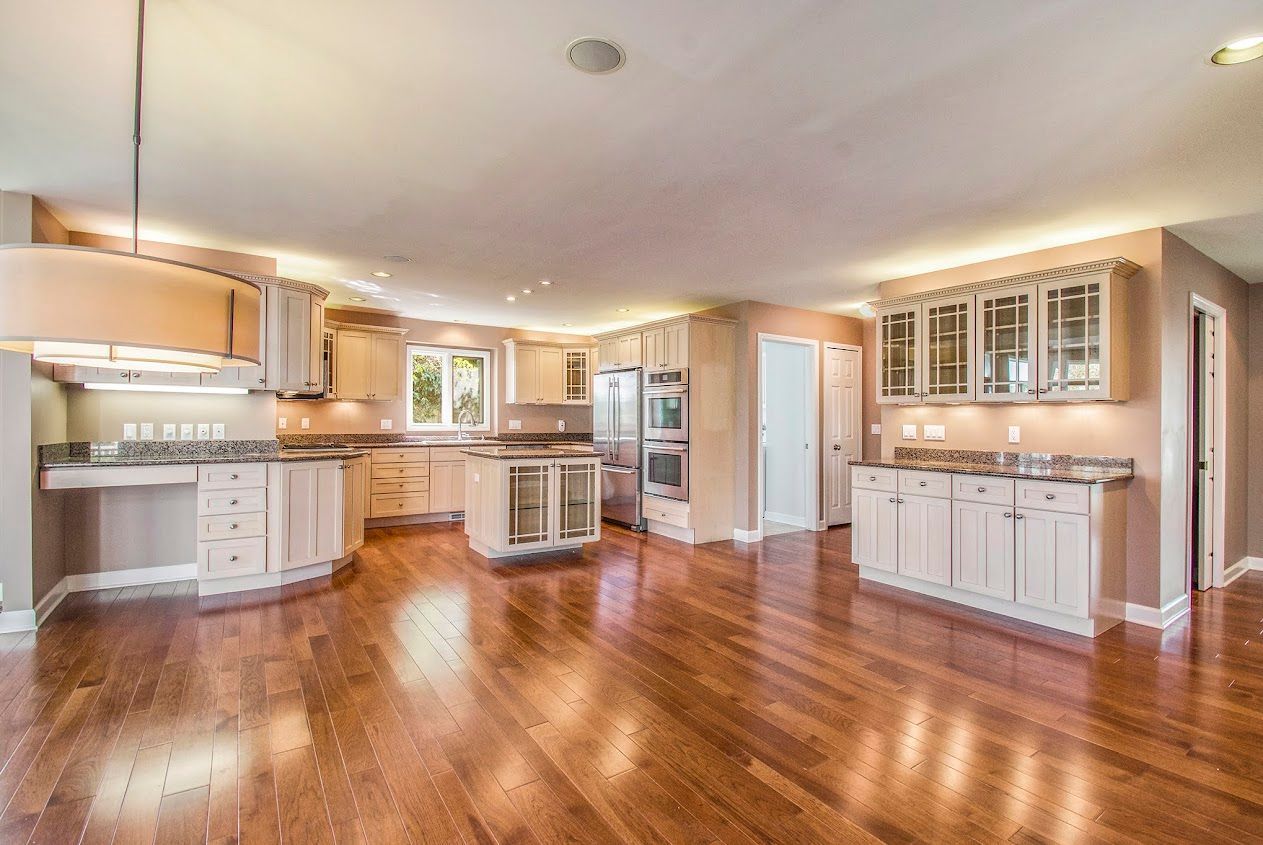 Spacious modern kitchen with white cabinets, stainless appliances, and glossy hardwood floors