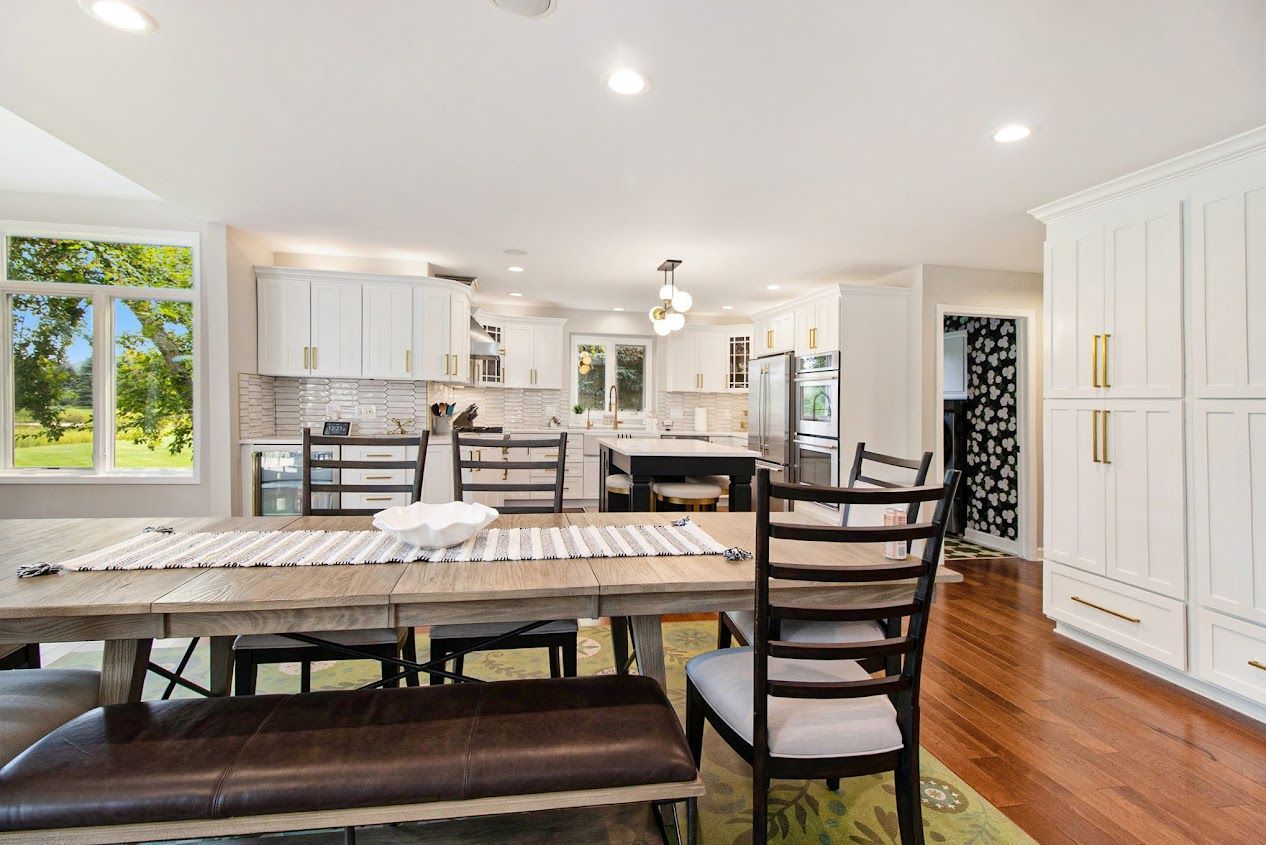Bright kitchen and dining area with white cabinets, wooden table, chairs, and green rug.
