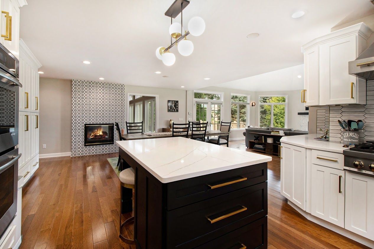 Bright modern kitchen with white cabinets, dark island, hardwood floors, and a fireplace in the dining area