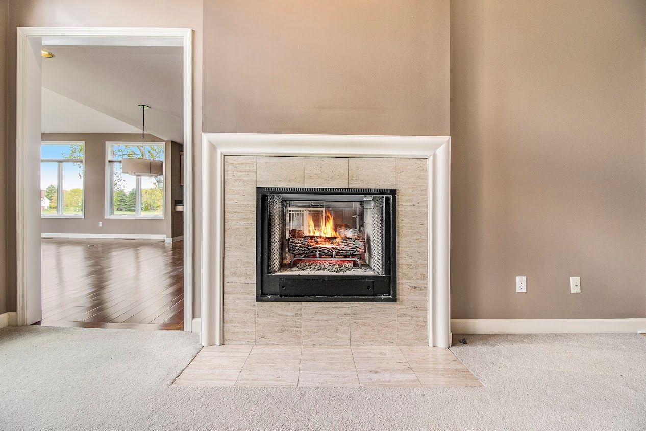 Living room with beige walls, white fireplace mantel, and a lit fire; doorway opens to another room.