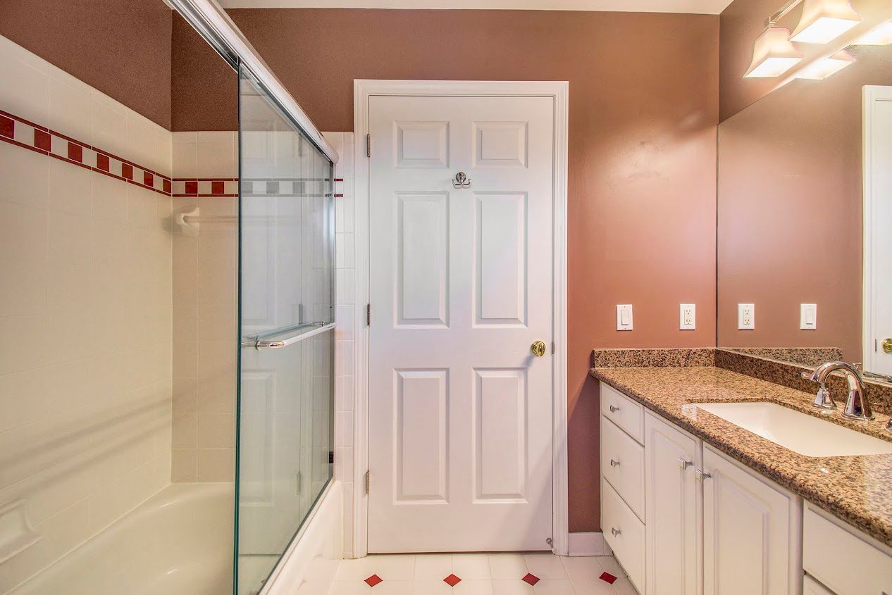Bathroom with glass shower, white door, and granite vanity against tan walls