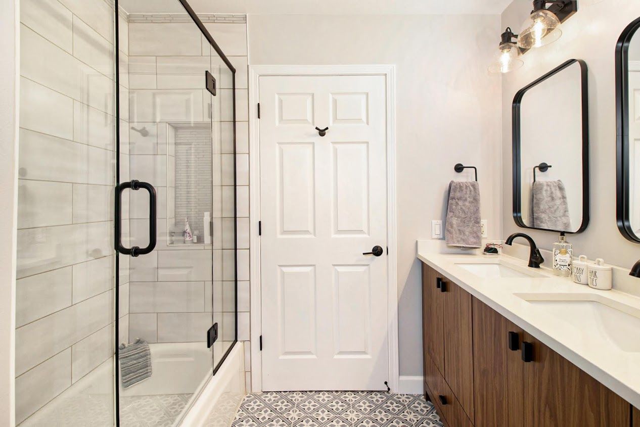 Bright bathroom with glass shower, white door, and dark vanity with sink and mirror