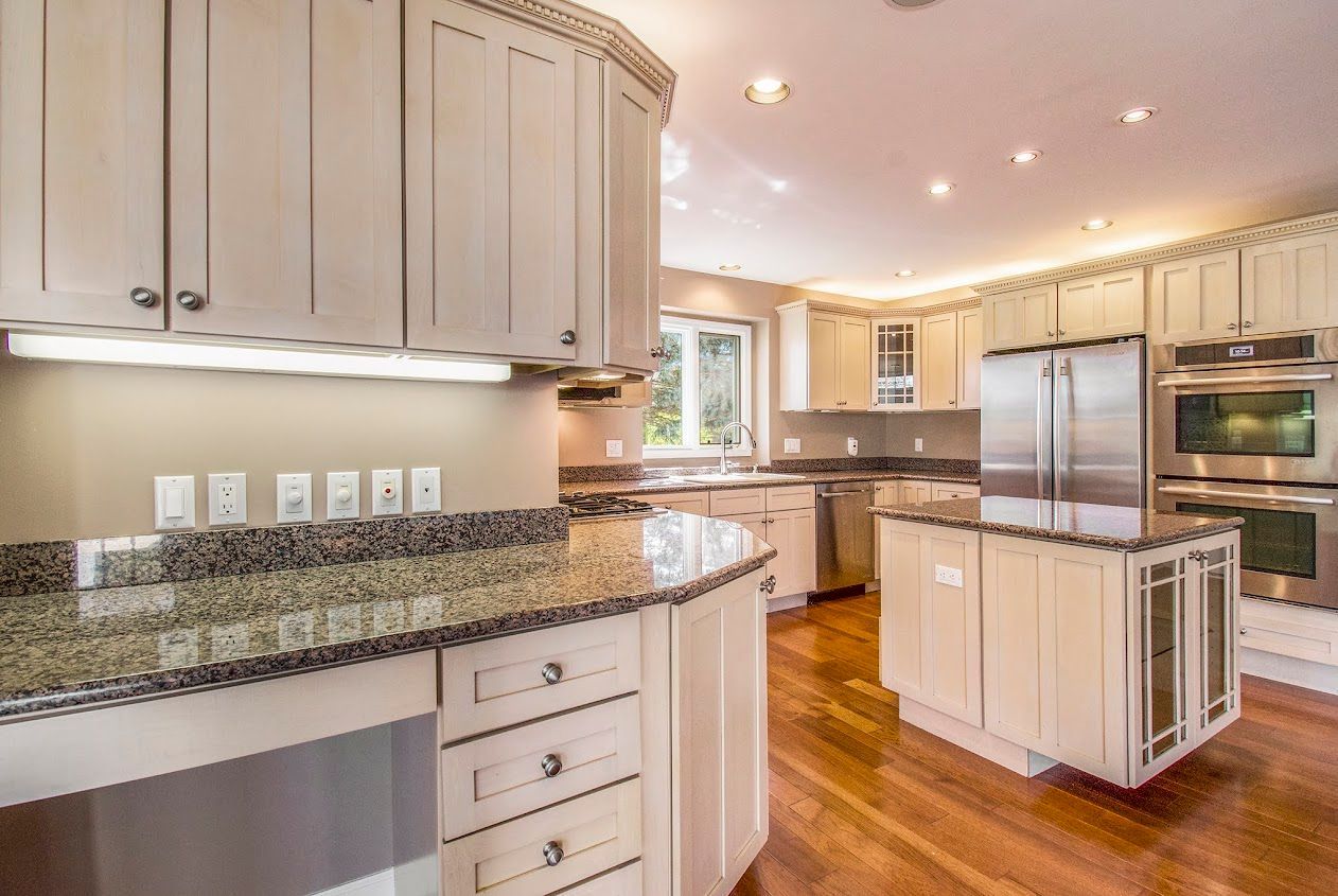 Bright modern kitchen with beige cabinets, granite counters, hardwood floors, and stainless steel appliances