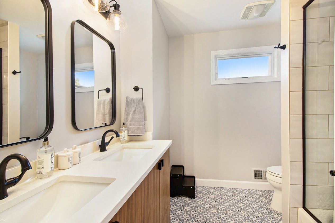Bright bathroom with double vanity, mirrors, white walls, pebble floor, and glass shower.