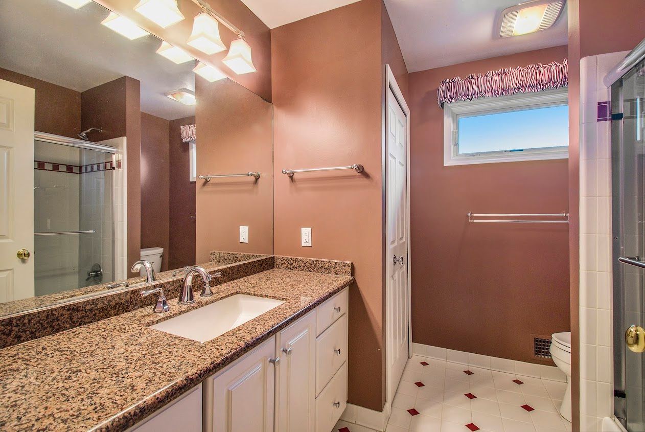 Bathroom with double sink vanity, granite countertop, mirrored wall, and walk-in shower.