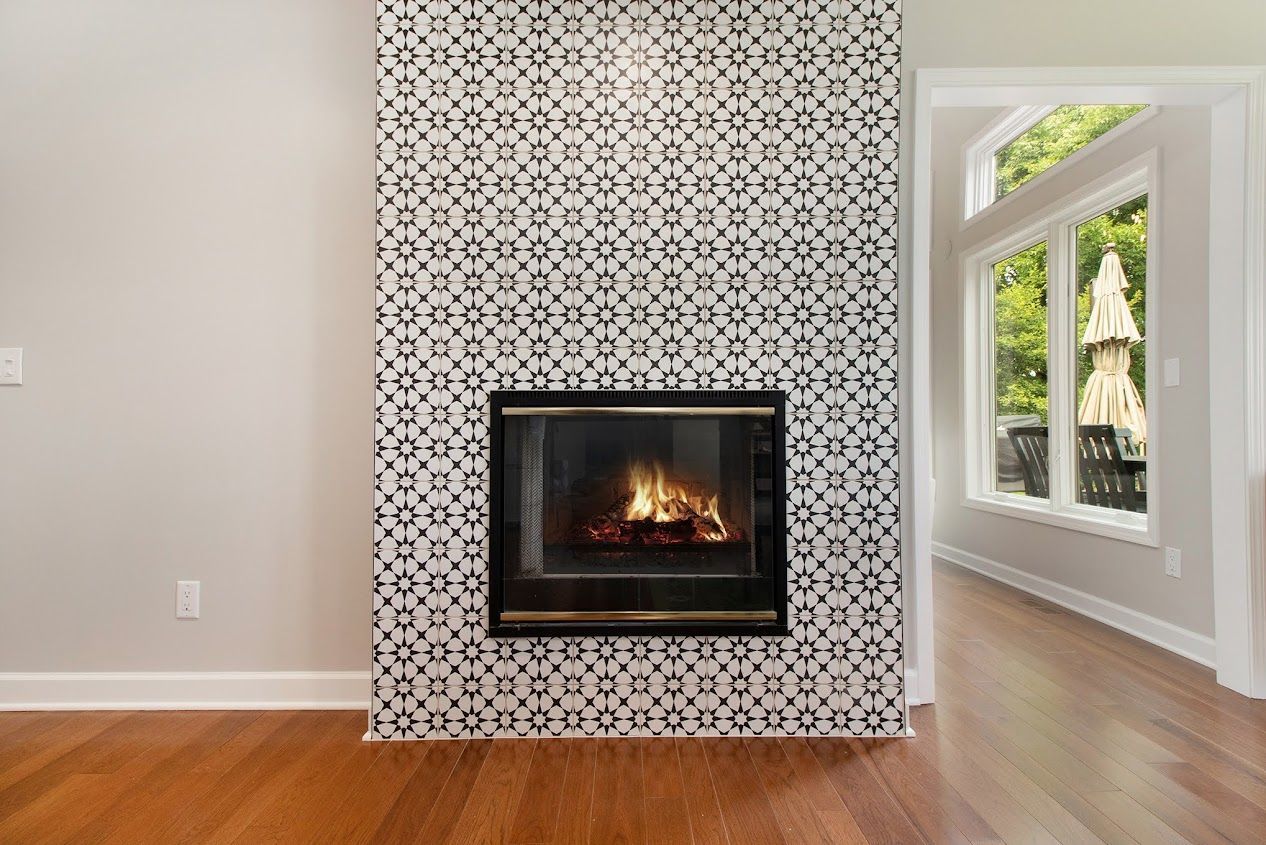 Modern living room with patterned fireplace surround, lit fire, hardwood floors, and large windows.