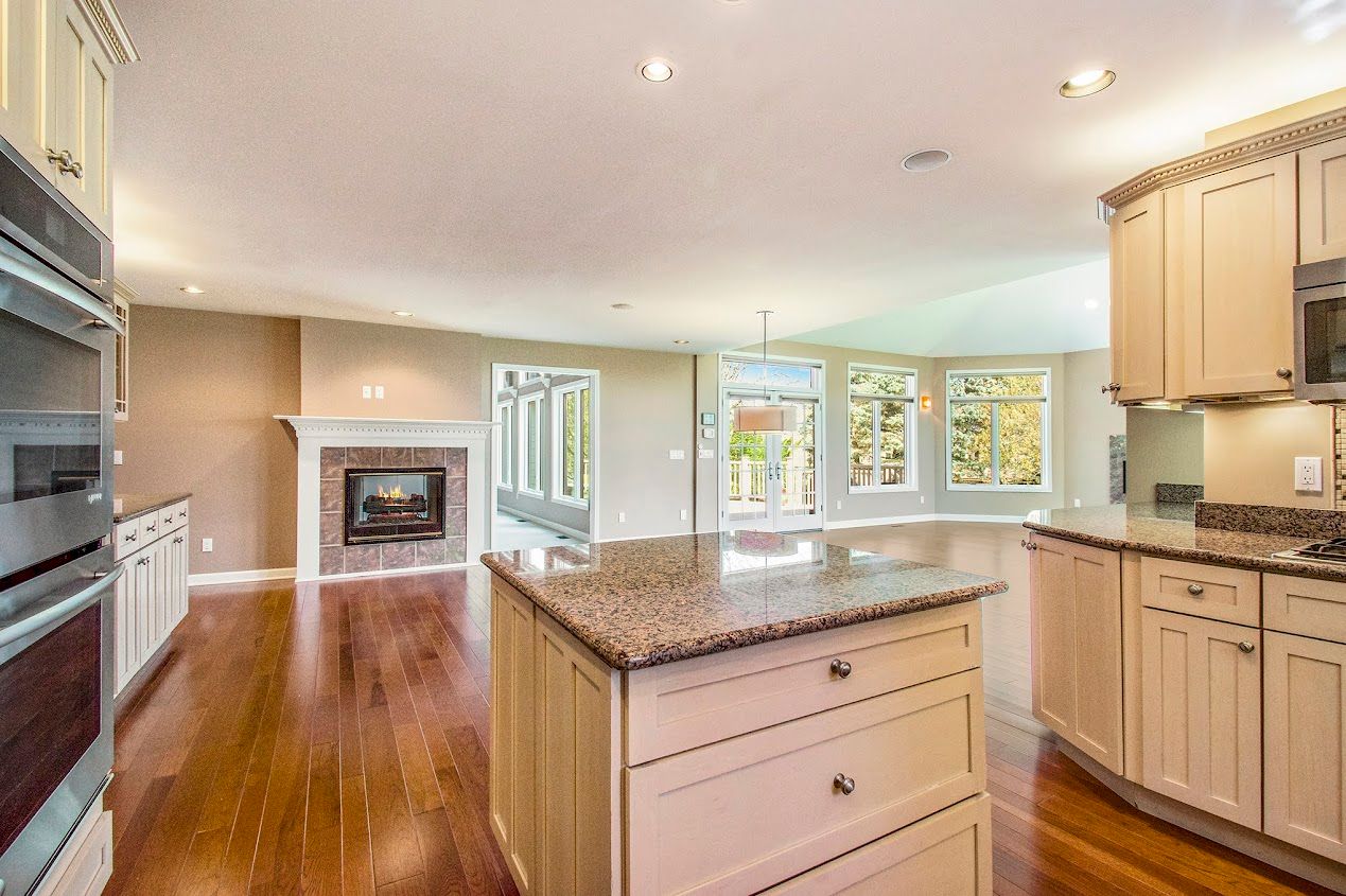 Bright kitchen with granite island, wood floors, fireplace, and large windows overlooking a backyard