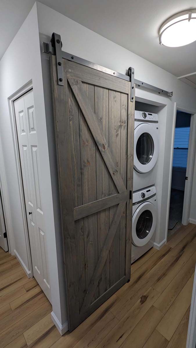 Laundry room with sliding barn door revealing stacked washer and dryer beside a hallway