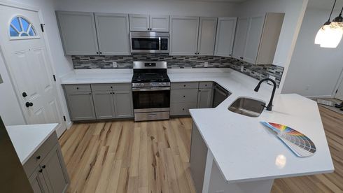 Modern kitchen with gray cabinets, stainless appliances, white island, and light wood floors