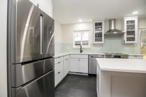 Modern kitchen with stainless steel appliances, white cabinets, and a central island with dark tile flooring