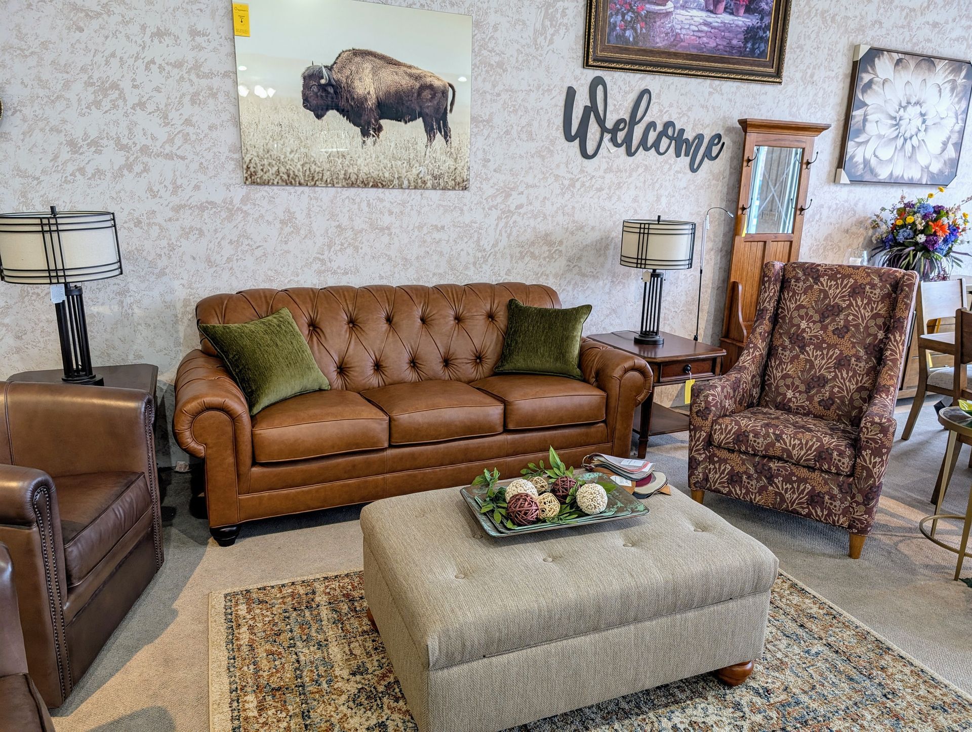 A living room with a couch , chairs , ottoman and a painting of a bison on the wall.