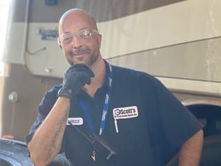 Mechanic in work clothes, smiling, resting hand on face, in front of a recreational vehicle.