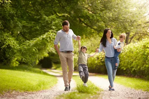 A family is walking down a path in the park holding hands.