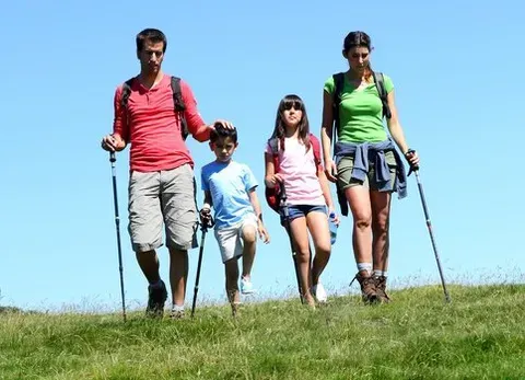 A family is hiking up a hill with walking poles.