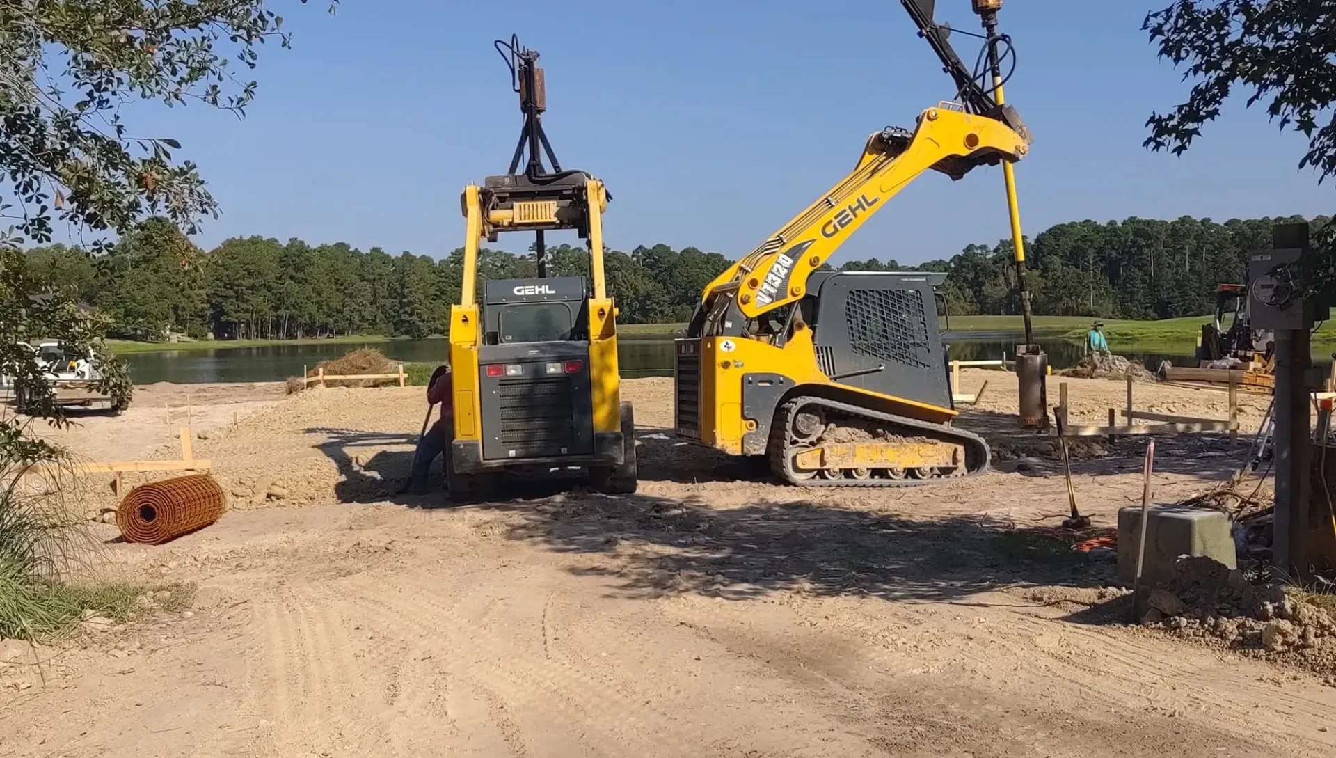 Yellow excavator and compact loader on a dirt construction site with trees in the background