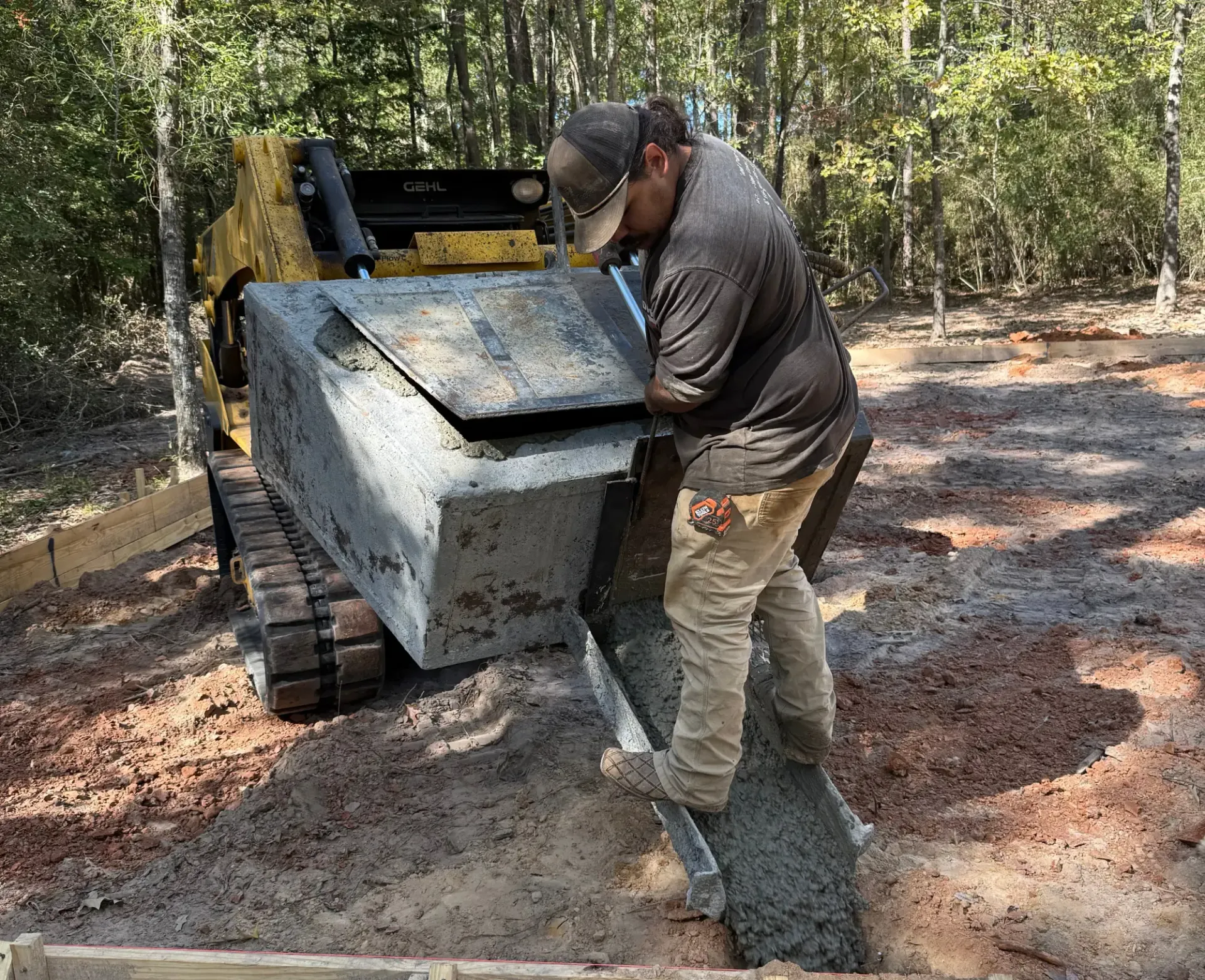 Man using a skid steer to dump gravel on a wooded dirt path
