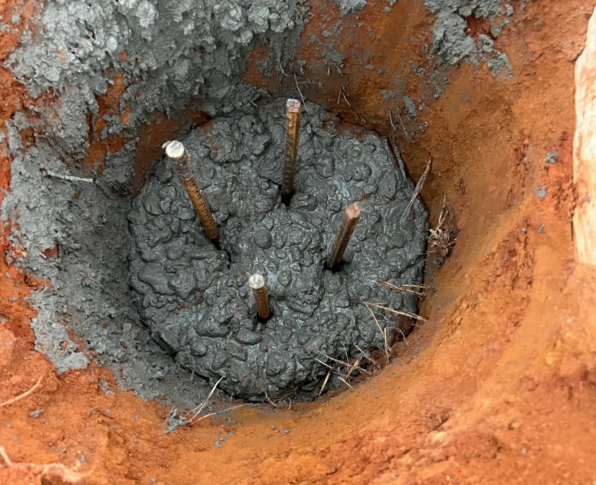 Concrete footing with four protruding rebar rods in an orange dirt excavation pit