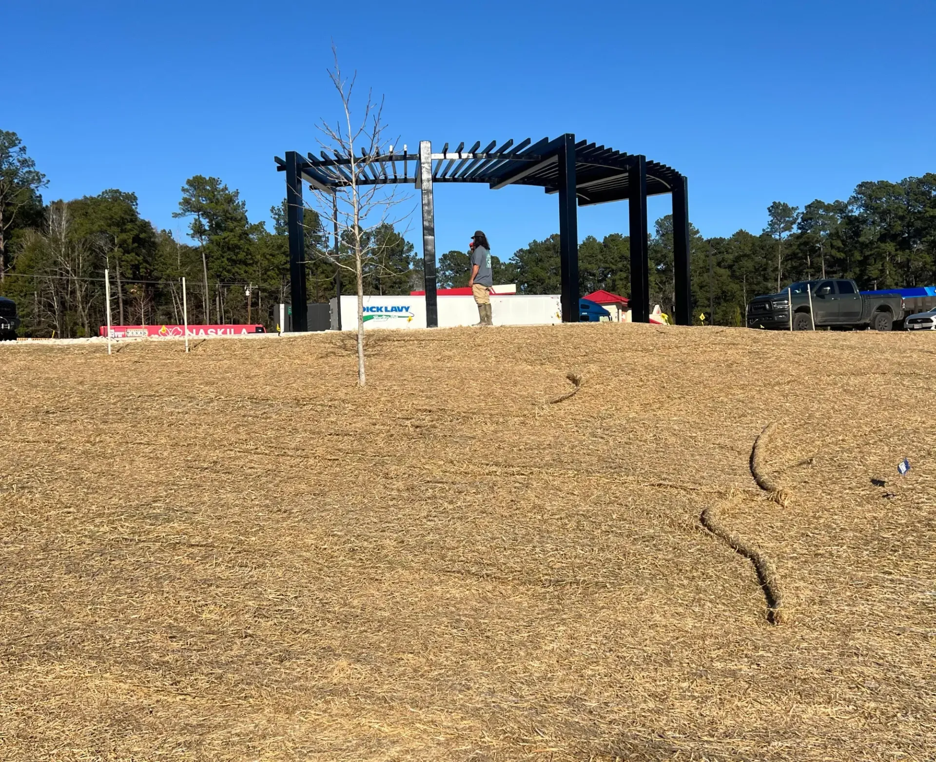 Wooden playground on a grassy hill under a clear blue sky with trees in the background