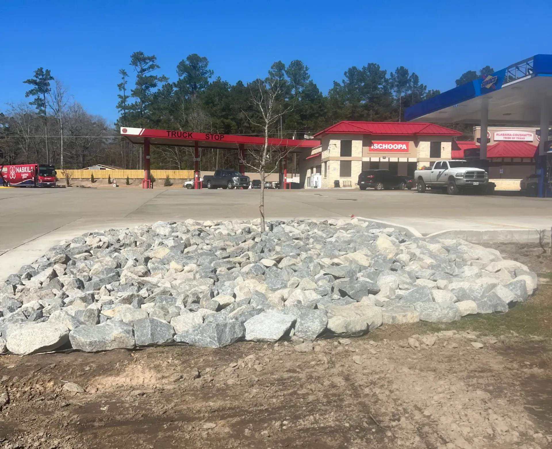 Large pile of white rocks in a parking lot near a gas station under a clear blue sky