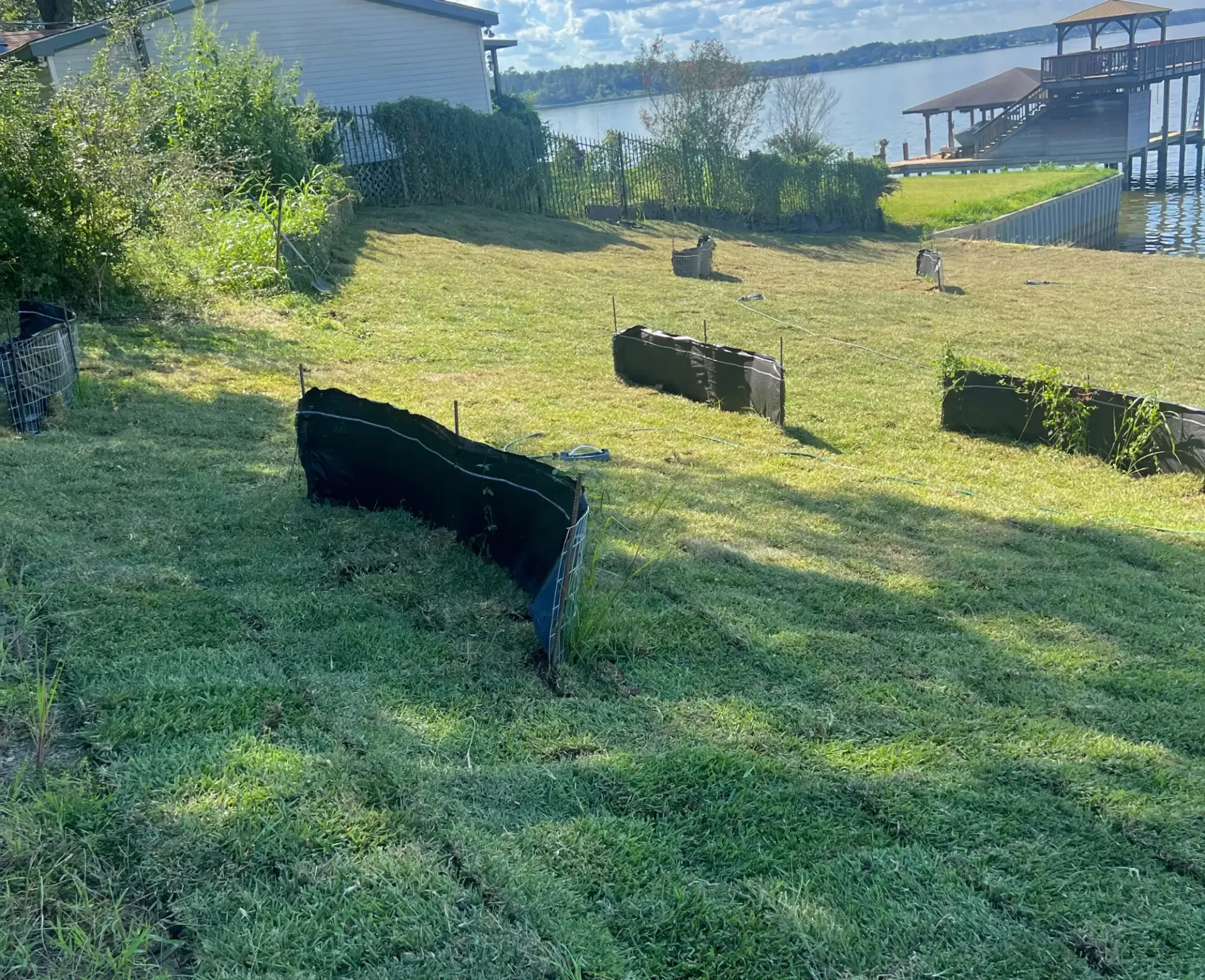 Grassy lakeside yard with black landscape barriers and a house in the background