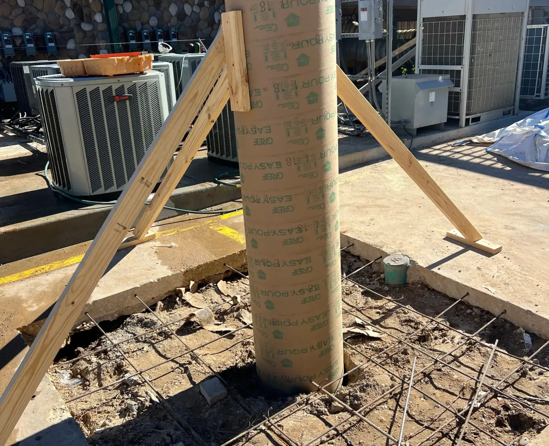 A wrapped utility pole supported by wooden braces on a snowy construction site.
