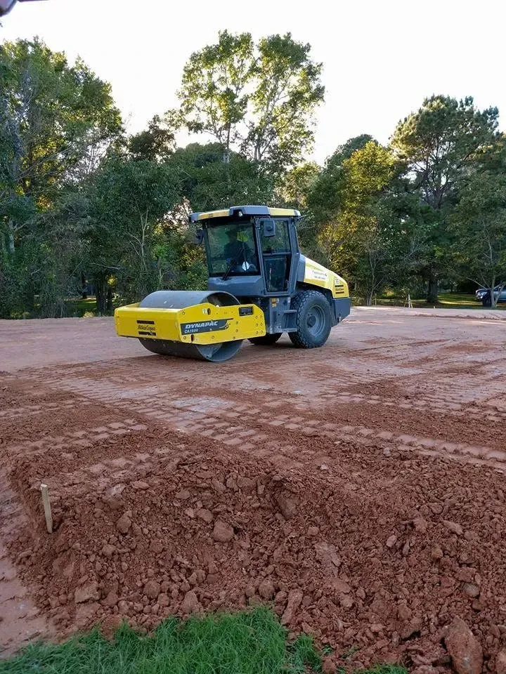Yellow road roller on a dirt construction site with trees in the background