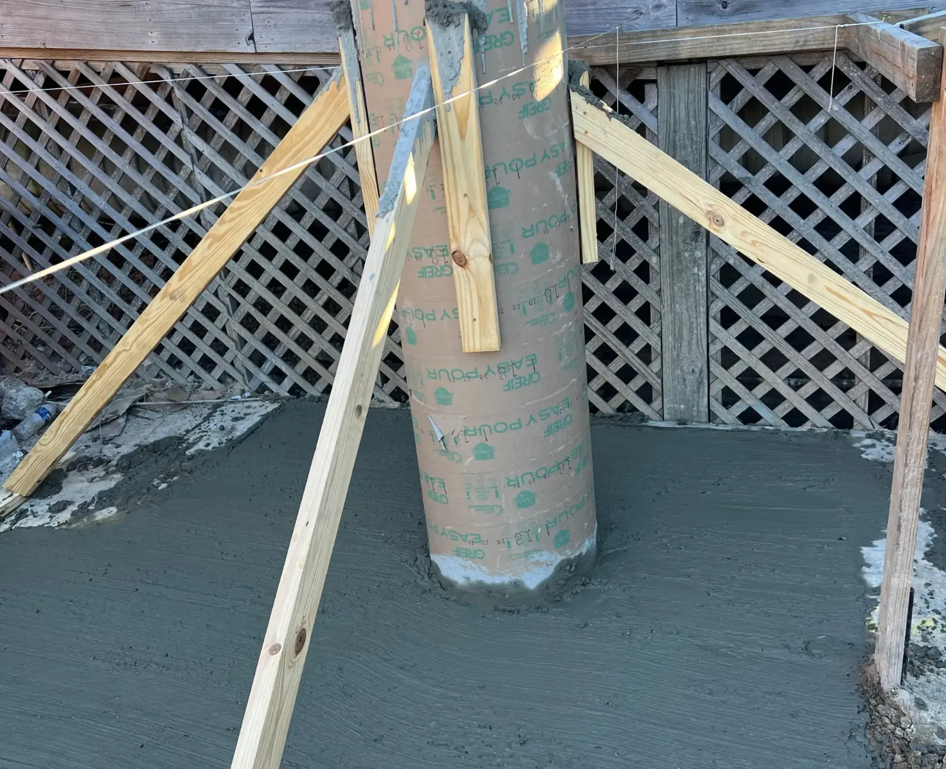 Concrete pillar being poured and supported by wooden braces on a construction site.