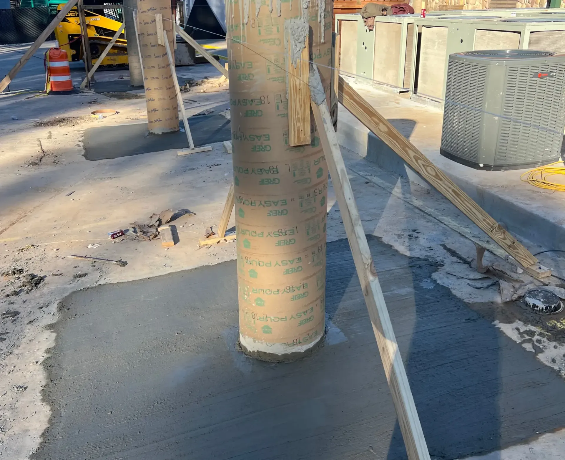 Construction site with wrapped columns, concrete floor, stacked materials, and safety barriers.