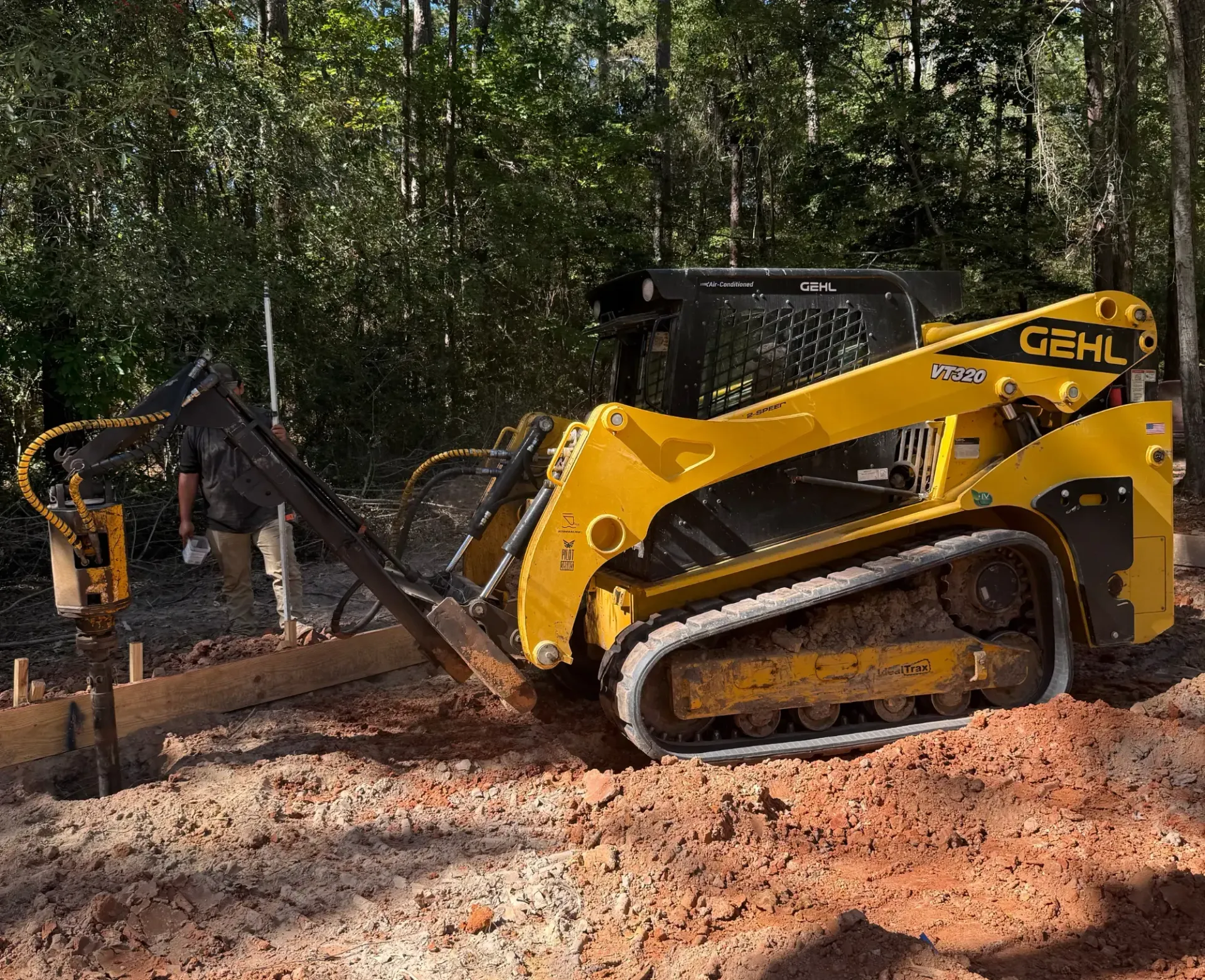 Yellow Gehl skid steer clearing mud in a wooded area