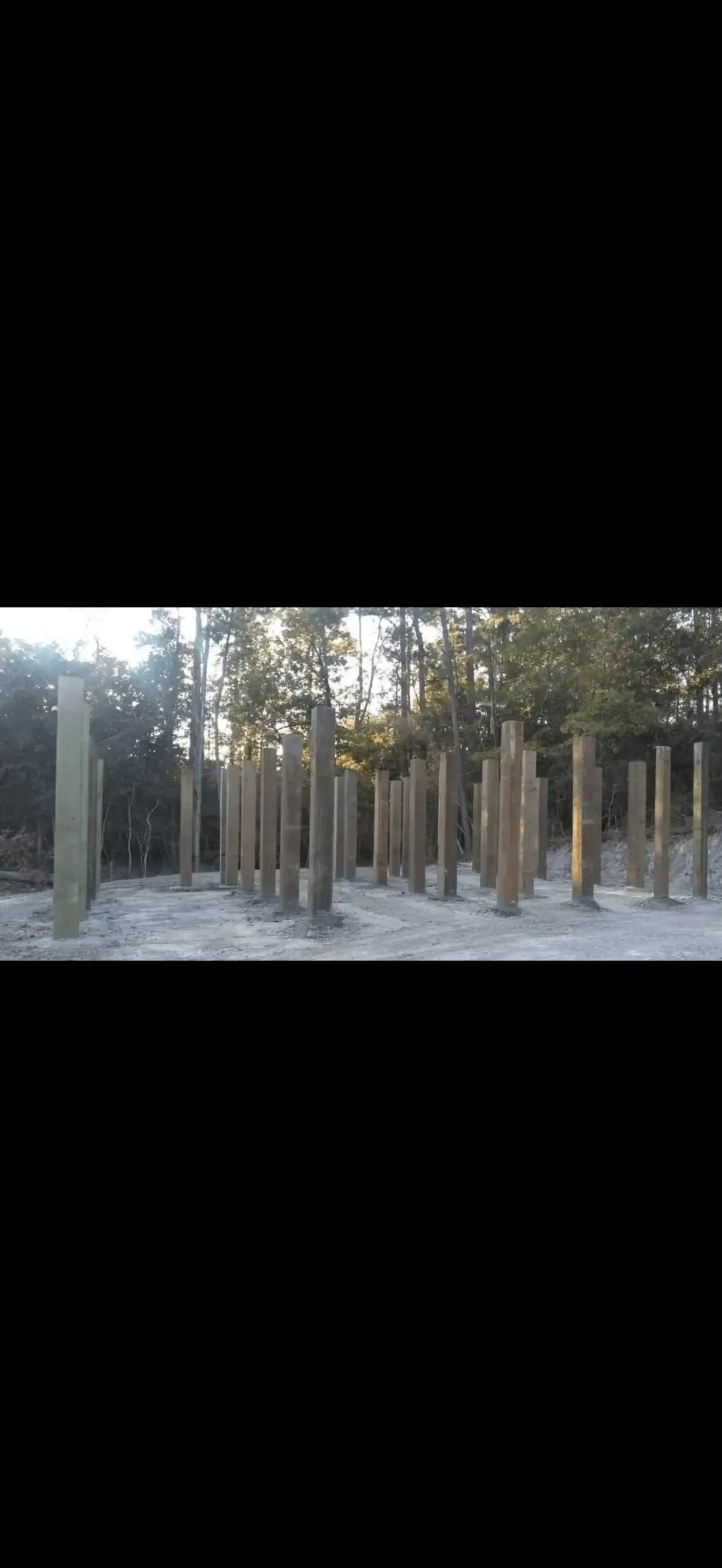 Empty park with tall concrete pillars and trees in the background at dusk
