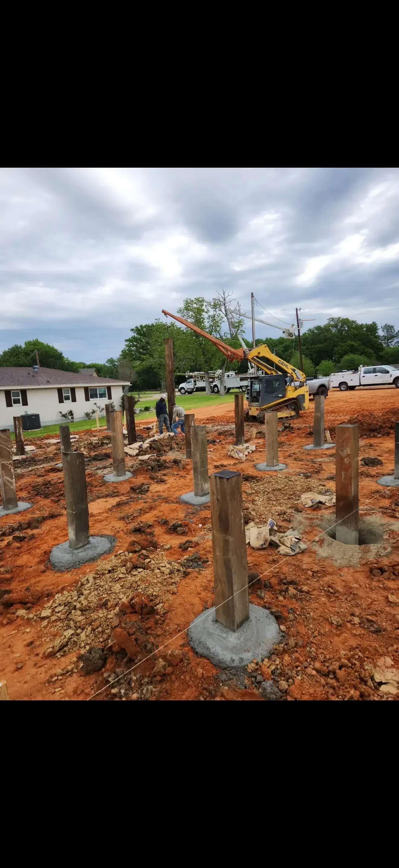 Construction site with concrete foundation piers and a yellow excavator under a cloudy sky