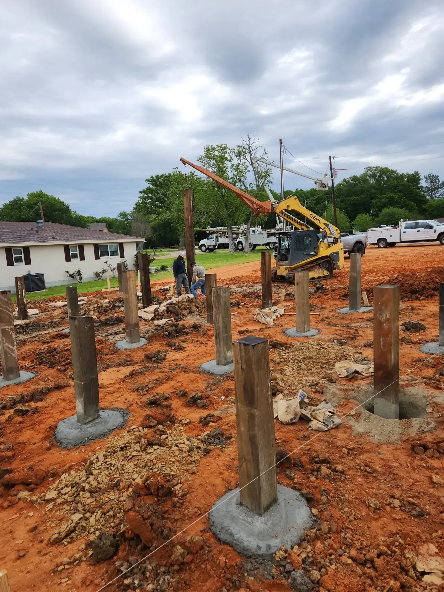 Construction site with concrete footings and a yellow excavator on muddy red soil