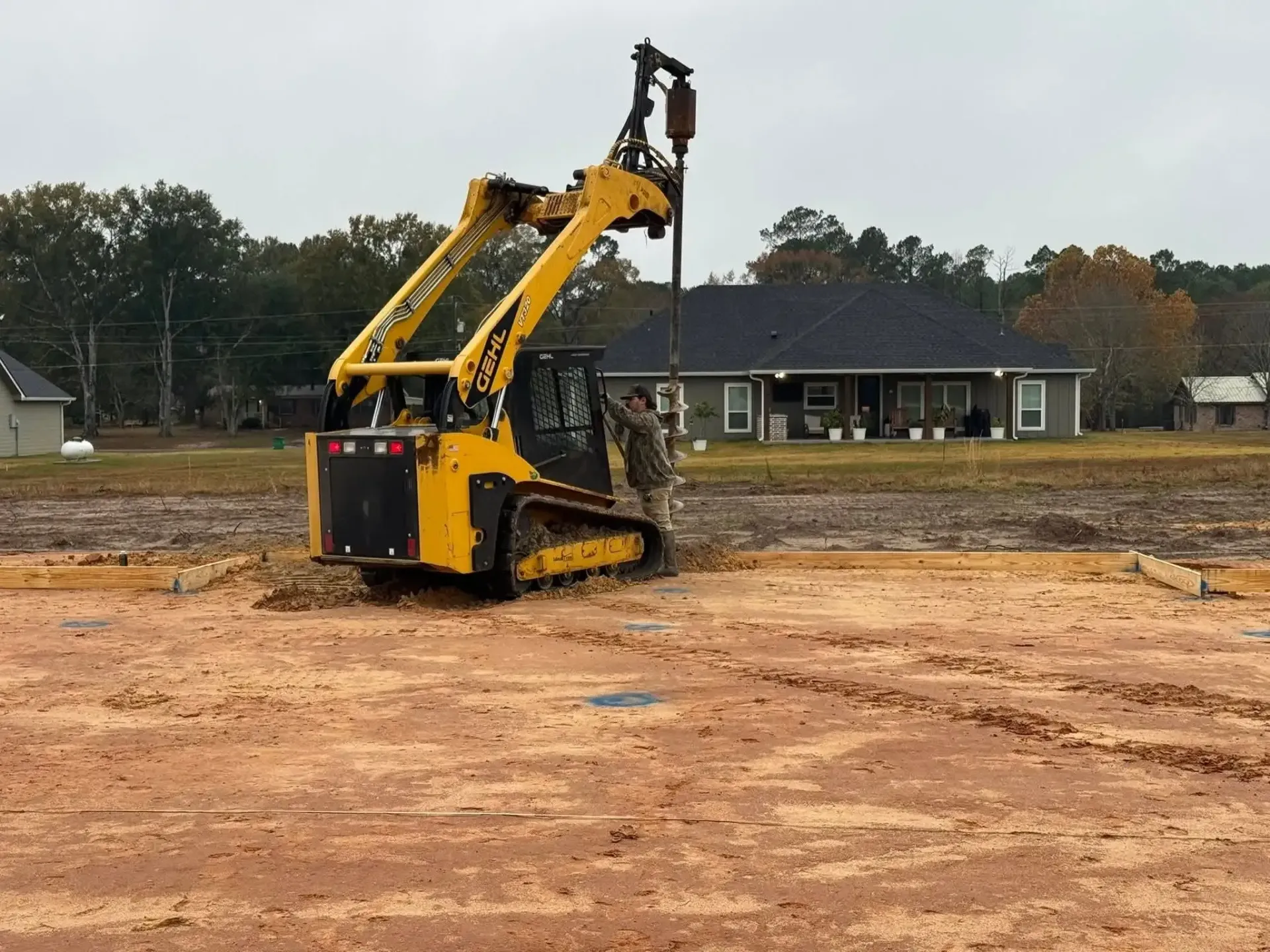Yellow excavator on a muddy construction site with a house in the background