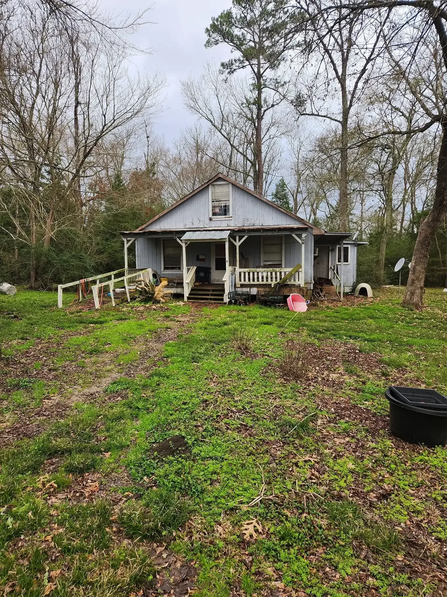 Small white house with a front porch and steps, set in a grassy yard with trees and overcast sky.