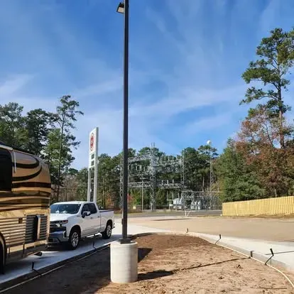 White pickup truck beside a roadside lot with a lamppost, blue sky, trees, and a wooden fence.