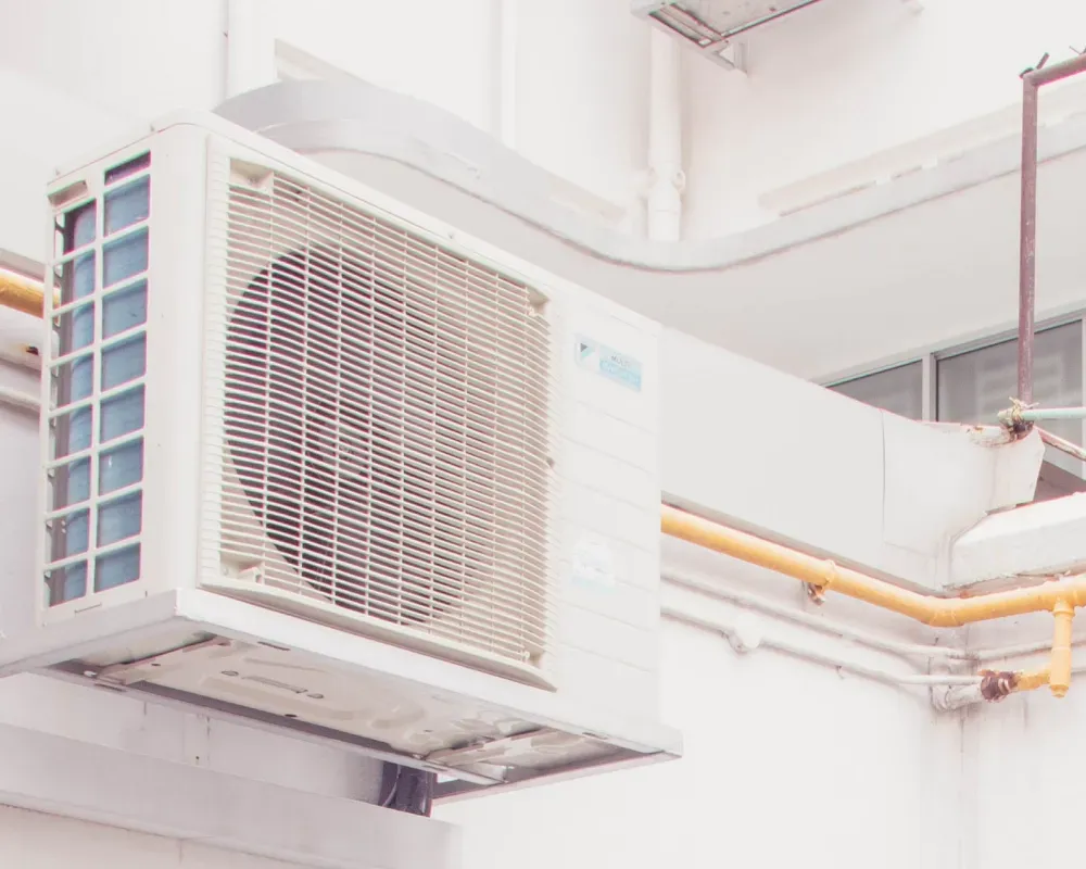 A white air conditioner is hanging from the side of a building.