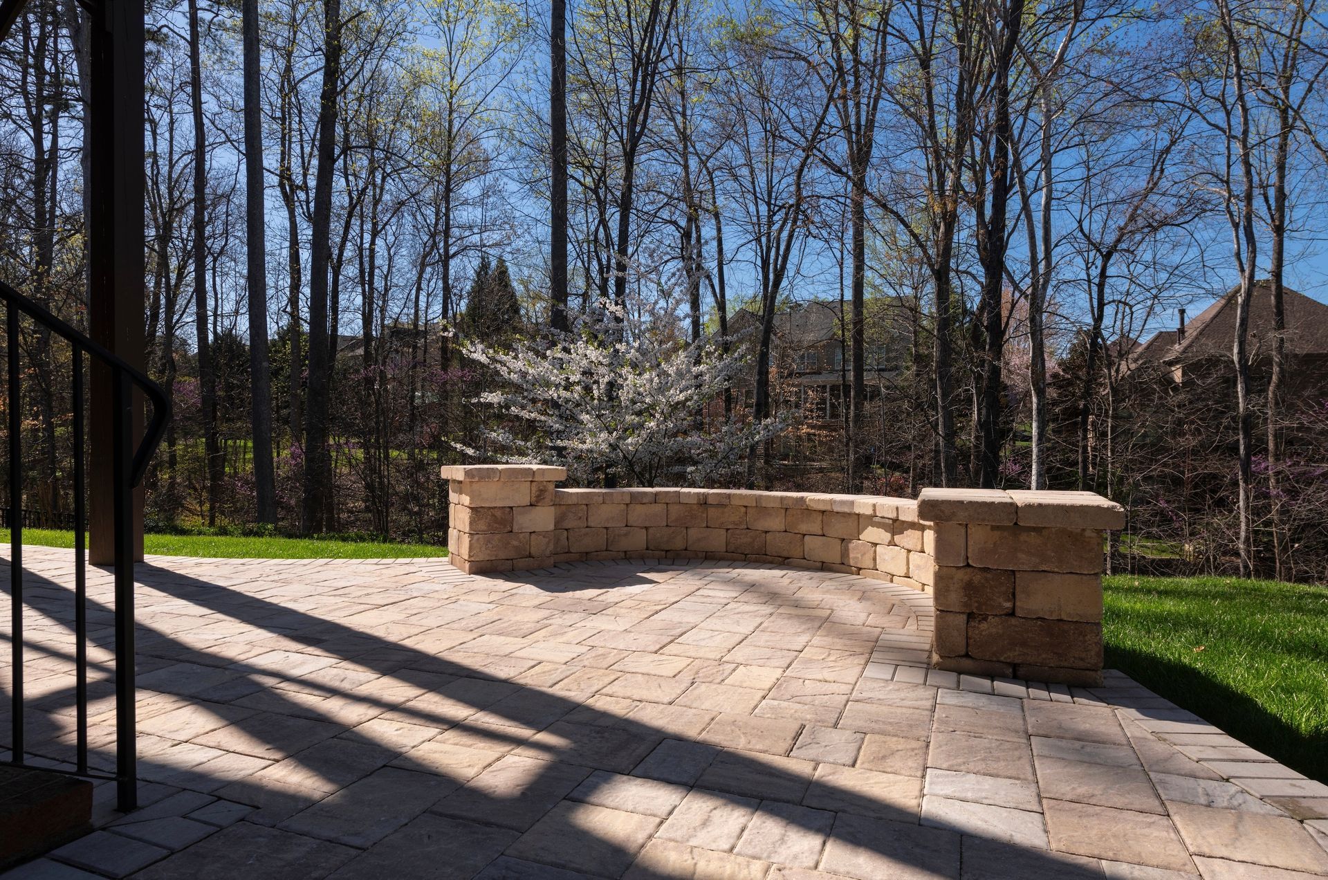 Stone patio with retaining wall, surrounded by trees and grass, under a sunny sky.