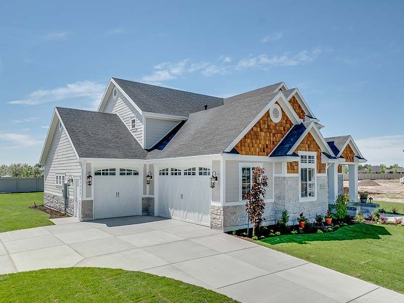 Gray house with white garage doors, brown cedar shake accents, green lawn, and blue sky.