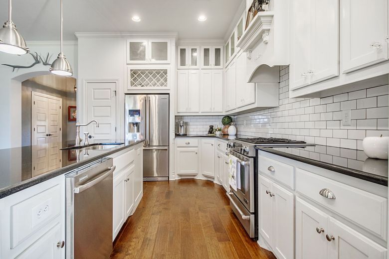 Bright white kitchen with stainless steel appliances, dark countertops, and hardwood floors.
