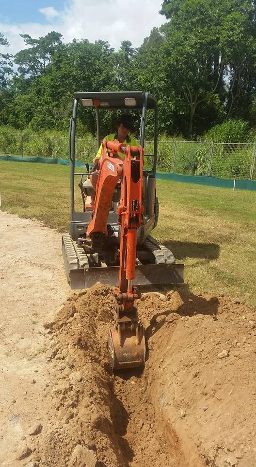 A Man Is Driving A Small Excavator In A Dirt Field — Absolute Dingo Services in White Rock, QLD