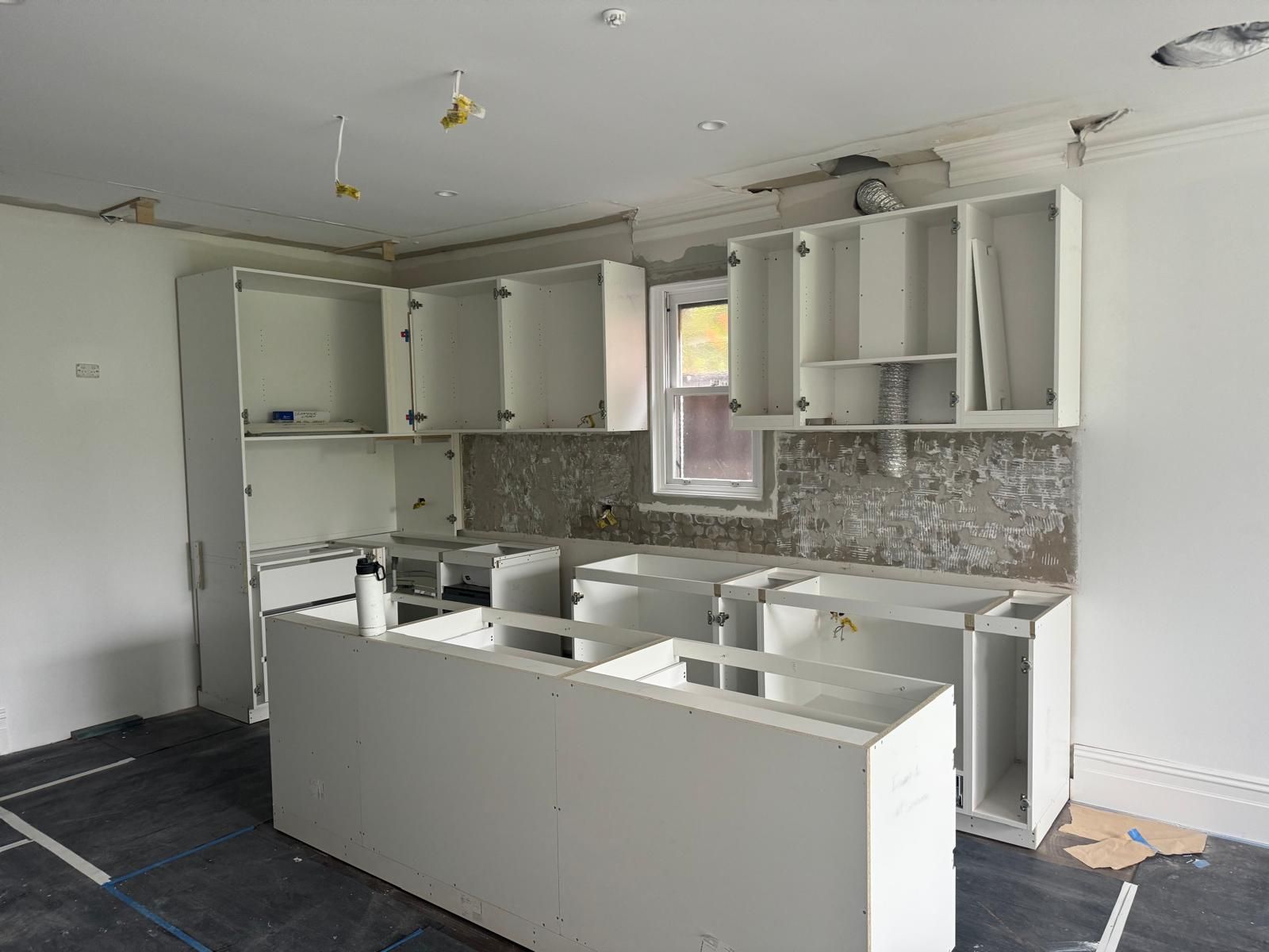 Kitchen under renovation with white cabinets, backsplash, and island.
