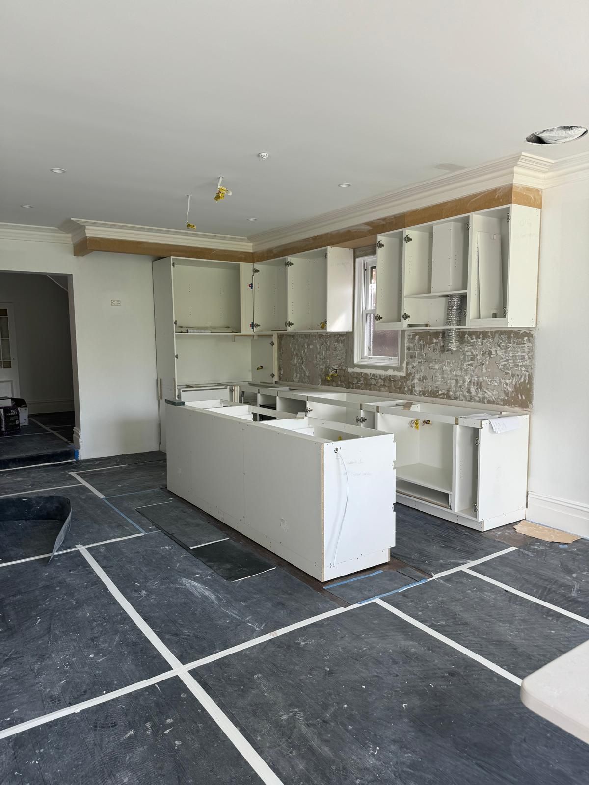 Kitchen under construction, white cabinets, island, backsplash, dark tiled floor.