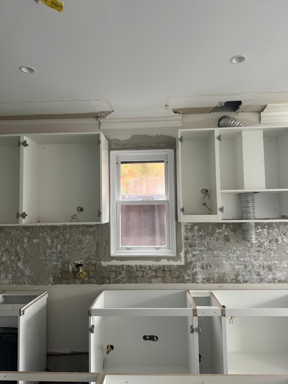 Kitchen under renovation; cabinets installed, backsplash removed, window in center. White cabinets, neutral walls.