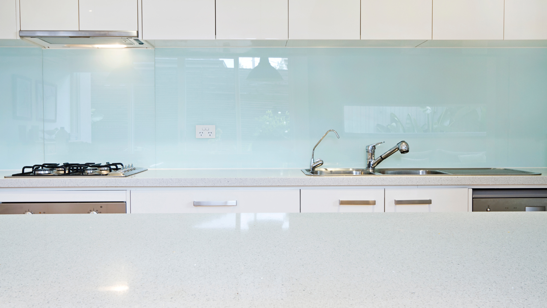 White kitchen counter with a cooktop, sink, and light blue backsplash.