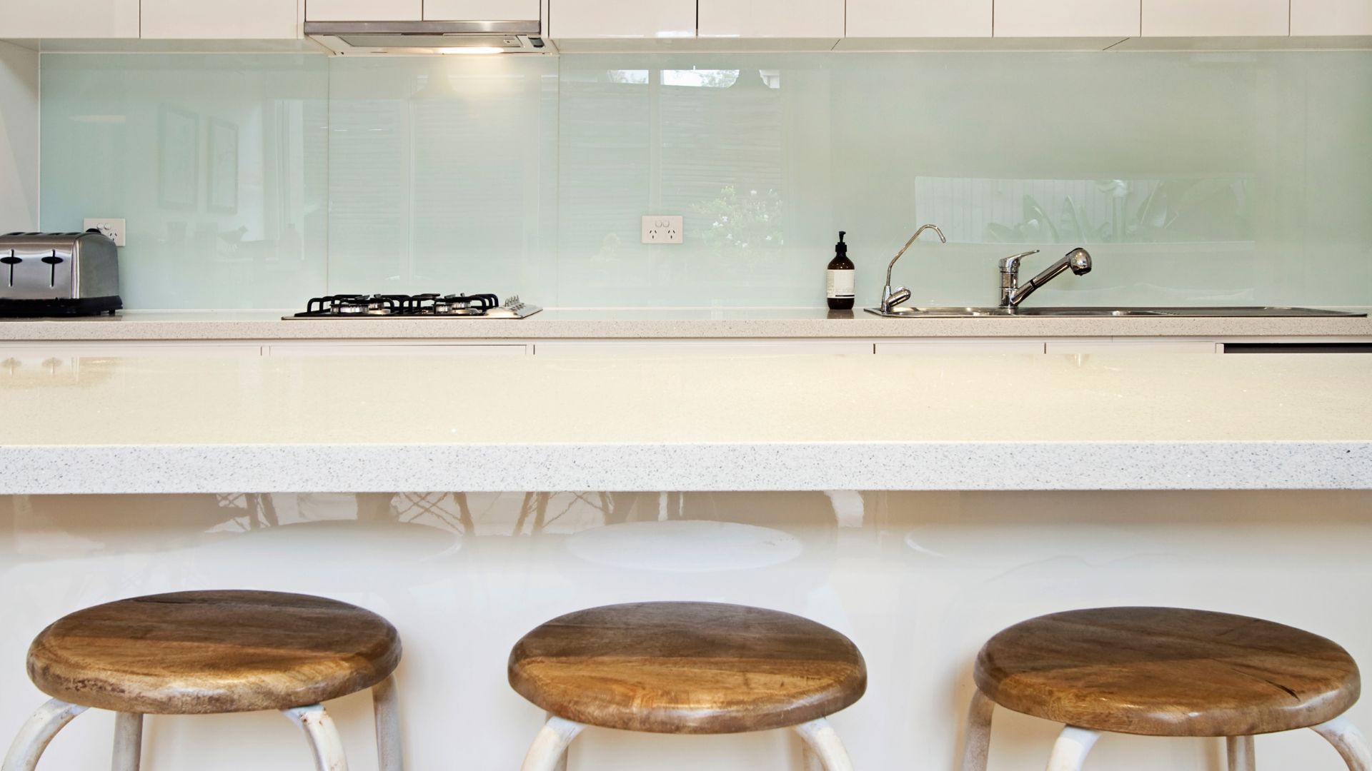 Three wooden stools in front of a kitchen counter with appliances and a sink.
