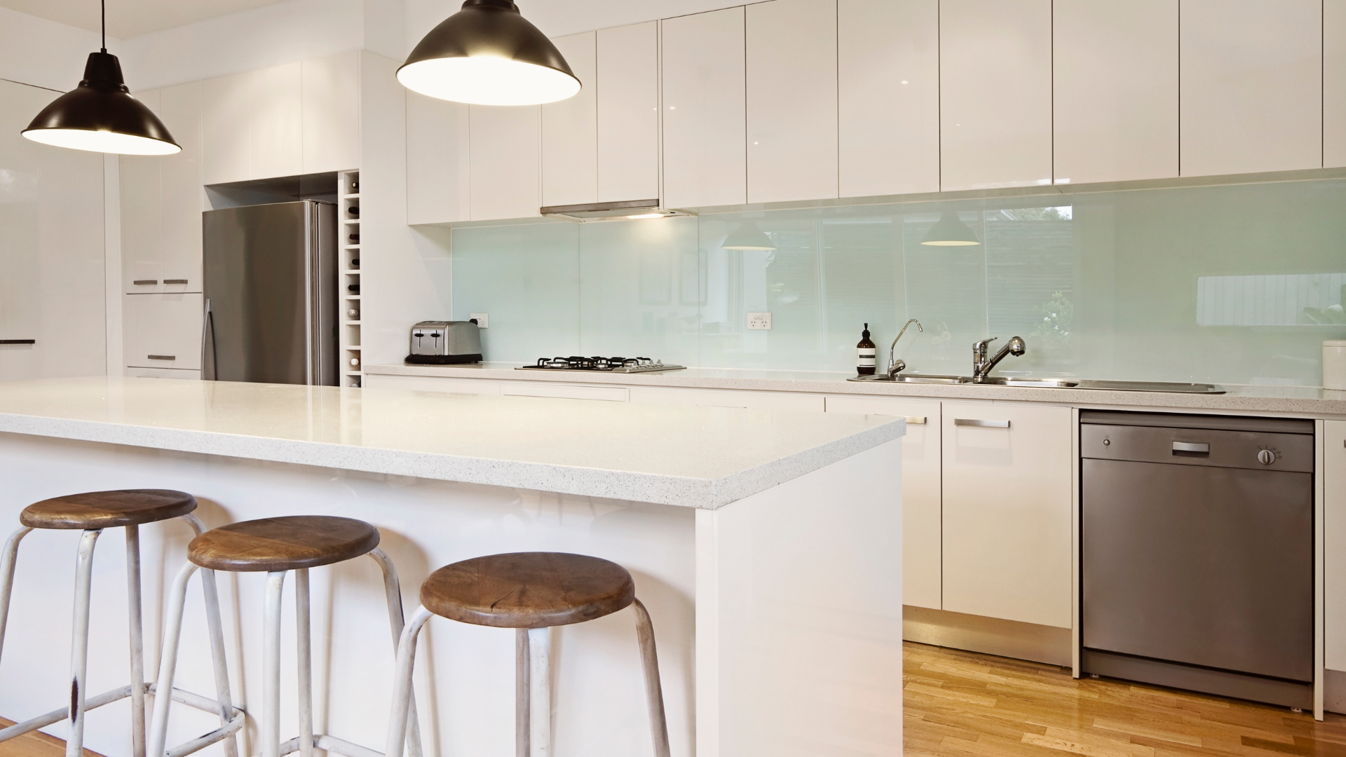 Modern white kitchen with a breakfast bar, stools, and stainless steel appliances.