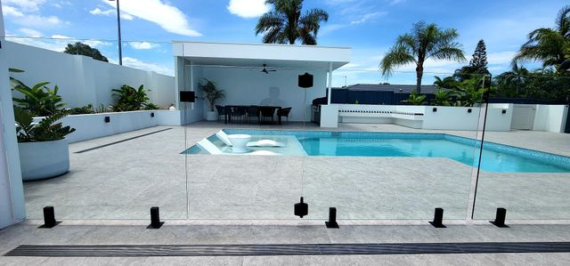 A modern outdoor pool area with a white cabana, blue sky, and glass fencing.