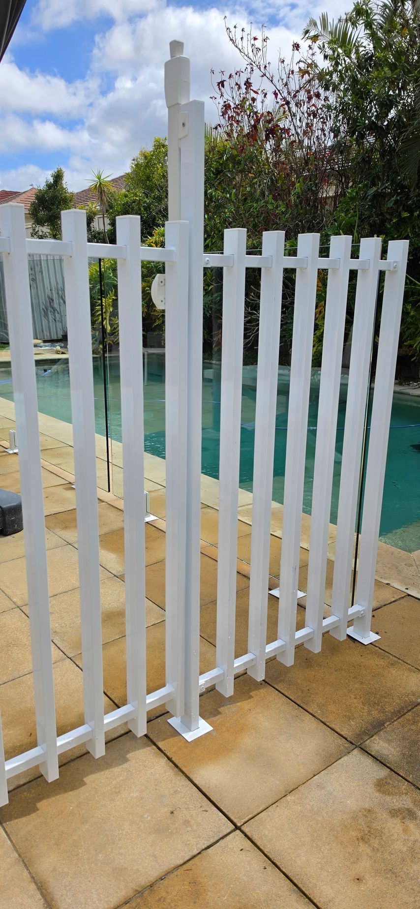 White pool fence beside turquoise water and tan stone patio