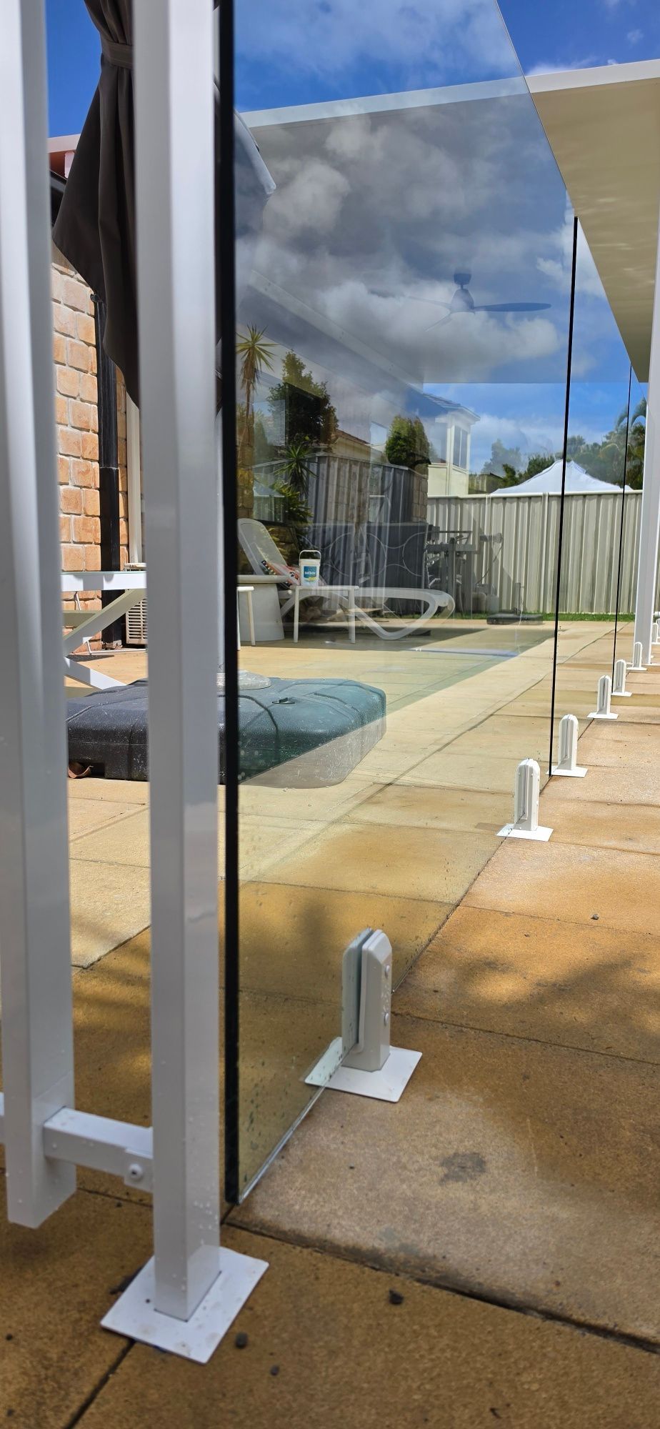 Glass windbreak panels beside a pool deck under a partly cloudy sky