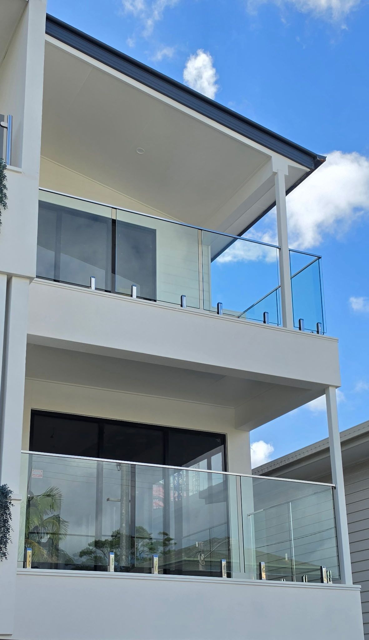Modern white two-story house with large glass balconies under a bright blue sky